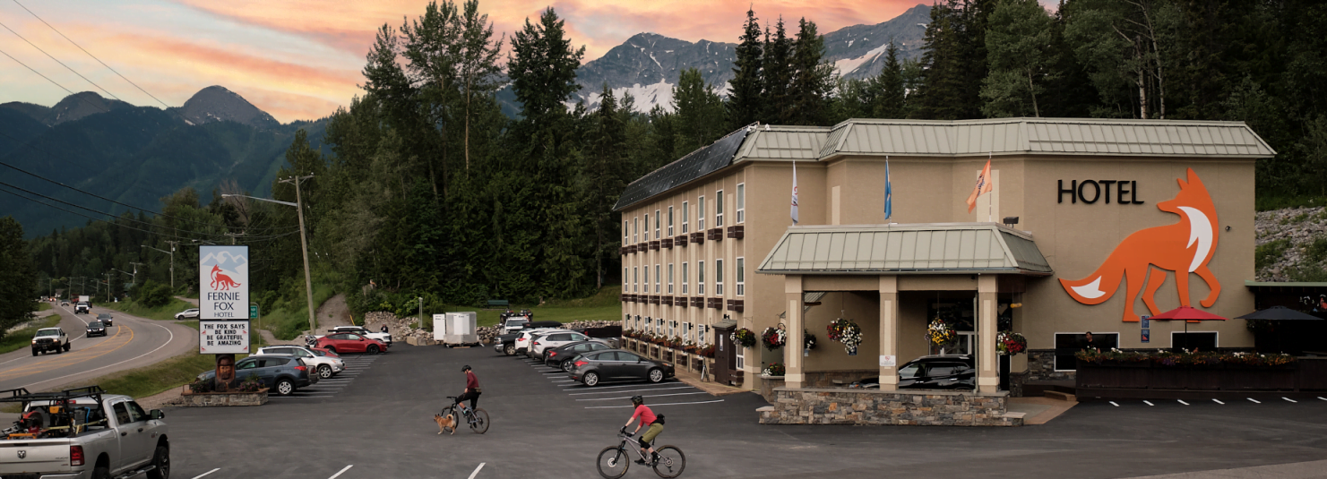 Fernie Fox Hotel with two bikers pedaling through the parking lot at sunset.