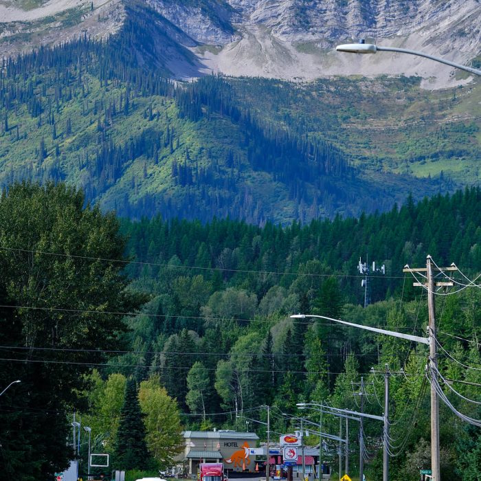 Fernie Fox Hotel along Hwy 3 in Fernie during the spring, the best time of year to visit Fernie. Cars driving down road, people cycling and walking along foot path.