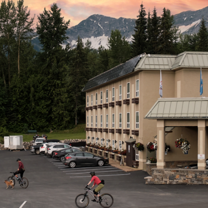Fernie Fox Hotel with two bikers pedaling through the parking lot at sunset.